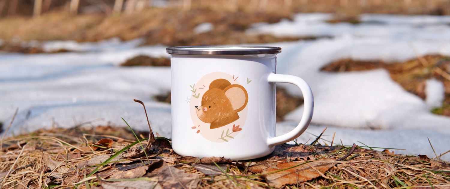 A children's mug with a bear placed on some leaves.